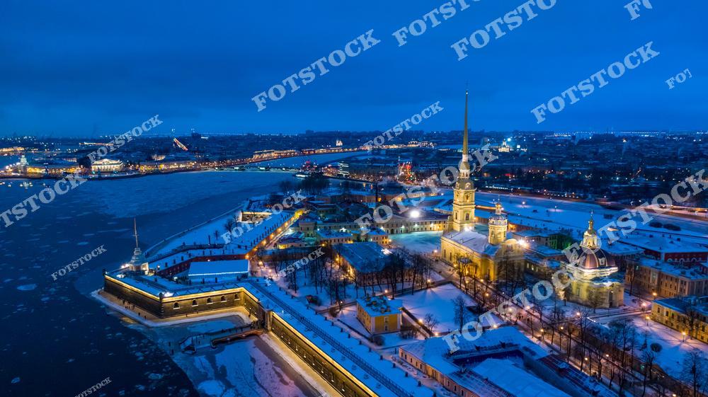 Панорамная фотография центра Санкт-Петербурга с высоты птичьего полета, снятая в вечернее время. На снимке видна Петропавловская крепость, собор Петра и Павла, крепостная стена, река Нева и протекающие по городу каналы. Съемка с дрона позволяет увидеть масштаб исторического центра, панораму архитектурных ансамблей и величие Северной столицы России. Фотография передает атмосферу вечернего Петербурга, гармонию городской среды с водными пространствами и уникальную архитектуру крепости. Снимок идеально подходит для туристических публикаций, фотостоков, рекламы, оформления интерьеров и материалов о достопримечательностях Петербурга.
